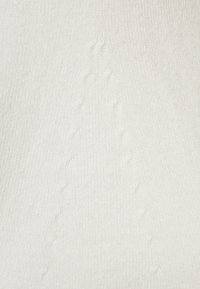 Vit stickad tyg med en texturerad mönstring och upphöjda prickar som skapar en subtil, dimensionell yta.