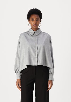 Cropped, light gray button-up shirt with a collar, drop shoulders, and a smooth texture. Paired with black trousers.