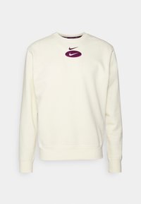 Krémová mikina z měkké látky, s kulatým výstřihem, žebrovanými manžetami a fialovým logem Nike uprostřed.