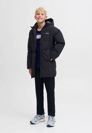 Musta toppatakki, jossa hupullinen, vetoketjullinen etuosa ja ruudukonmuotoinen tikkauskuvio. Päällä tummansinisen paidan kanssa, yhdistetty mustiin housuihin ja lenkkareihin.