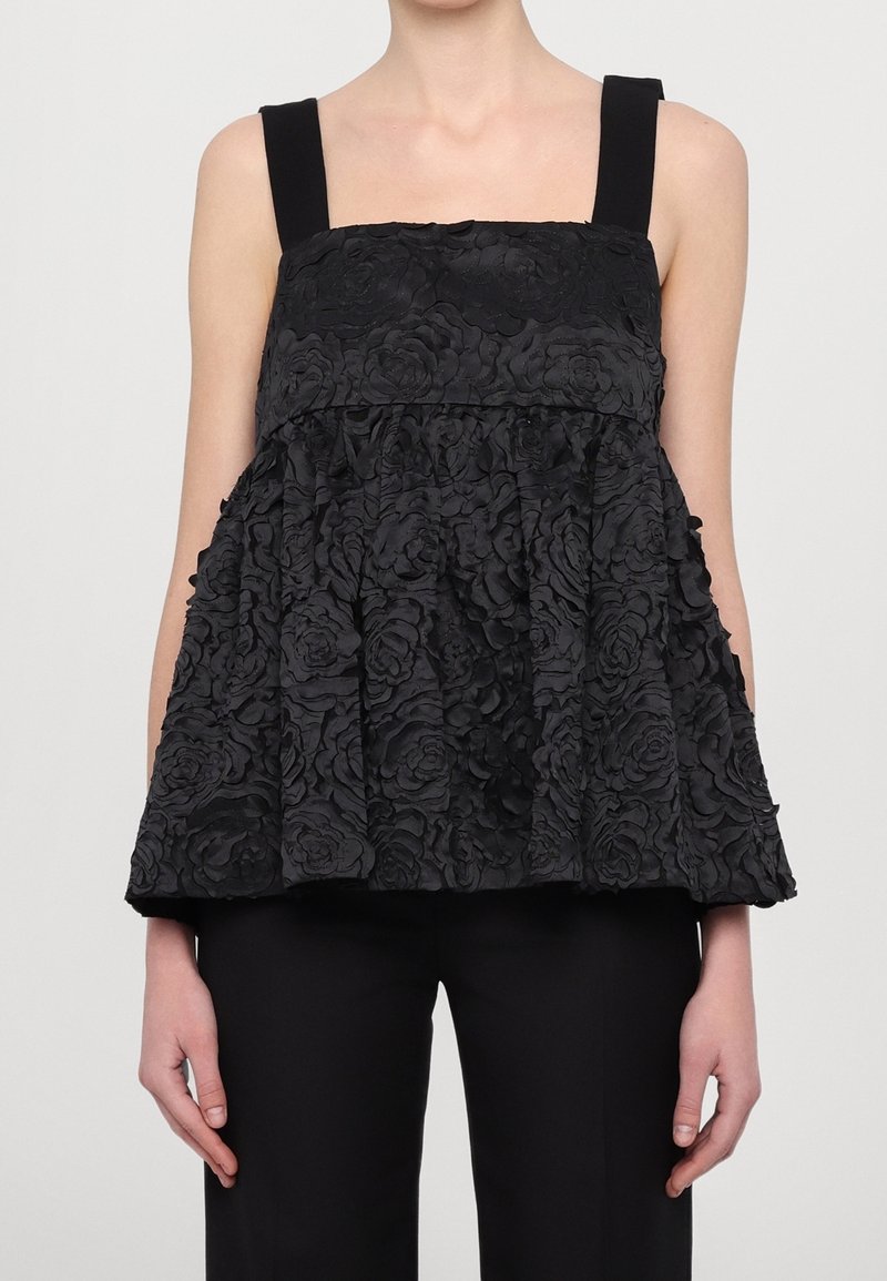 Top noir orné de motifs floraux avec des bretelles carrées, des motifs de roses texturés, et une silhouette évasée, associé à un pantalon noir.
