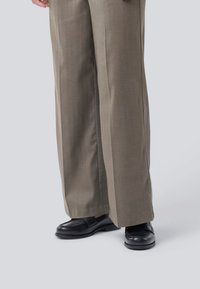 Pantaloni larghi khaki realizzati in un tessuto testurizzato, con una parte frontale pulita, abbinati a moccasini in pelle nera.
