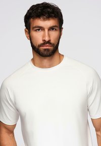 Hvid kortærmet t-shirt lavet af blødt stof med rund halsudskæring og raglanærmer, der har en glat tekstur og et minimalisk design.
