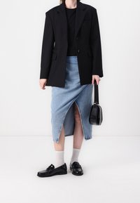 Svart blazer över en svart topp, tillsammans med en ljusblå denimkjol med en framficka. Svarta loafers och en liten svart handväska fulländar looken.