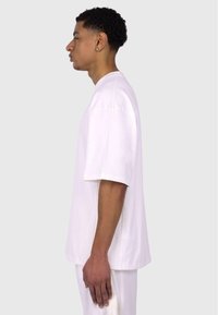 Hvid kortærmet t-shirt i et afslappet fit. Blødt stof, rund hals og synlige sidesømme. Modellen vist i profil mod en grå baggrund.