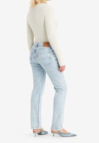 Ljusblå högmidjade jeans med avslappnad passform, med bakfickor och en tanfärgad läderlapp. I kombination med en texturerad ljusgrå långärmad topp.