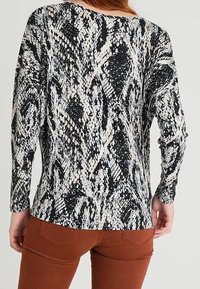 Długi rękaw bluzka w czarno-białym wzorze w węża. Wykonana z miękkiego materiału, posiada luźny krój i okrągły dekolt.