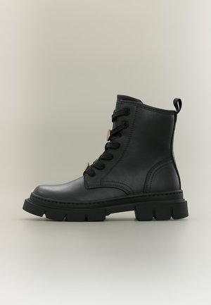 Botte de combat en cuir noir avec semelle en caoutchouc épaisse, lacets à l'avant et languette à l'arrière sur fond neutre.