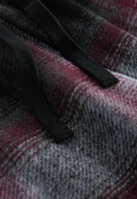 Károvaná fleecová tkanina v tmavě červené, šedé a černé barvě s černými stahovacími šňůrkami. Měkká textilie s viditelnou vazbou. Bez kovových detailů.
