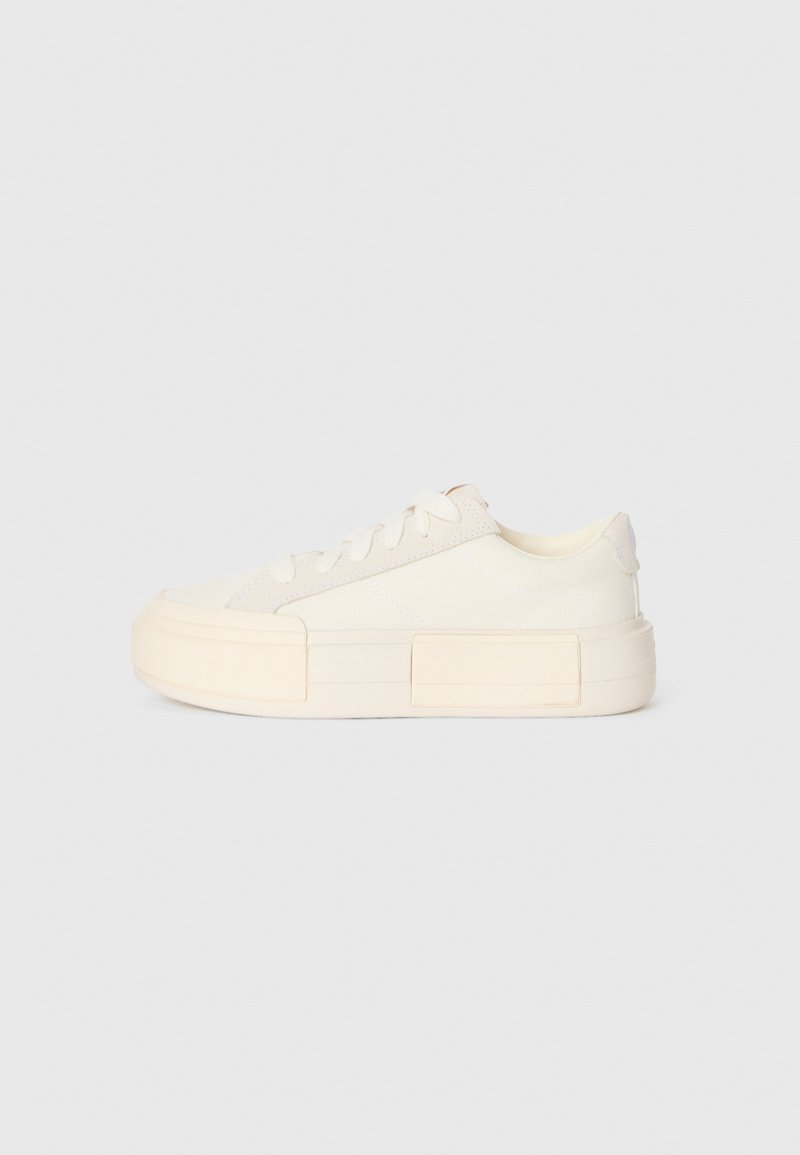 Lave toppen off-white sneakers med chunky såle, snøredesign og minimale sømdetaljer, vist mot en ensfarget bakgrunn.