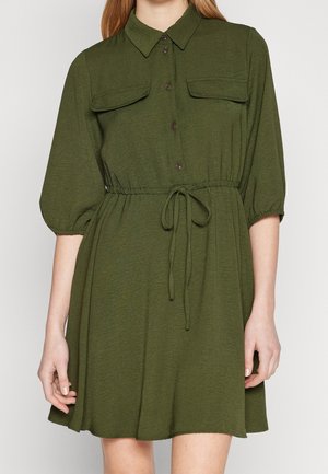 Kort olivengrøn skjortekjole med klaplommer på brystet, trekvart ærmer, elastisk talje og bindebånd med snor.