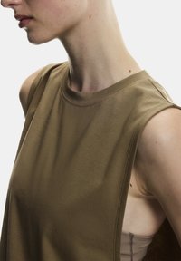 Bezrukávový hnedý bavlnený top s okrúhlym výstrihom, textúrovanou tkaninou a viditeľným detailom šitia. Dizajn má široké ramenné otvory.