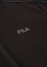 Tela de forro polar negra con textura suave, que presenta un logo de FILA en gris visible y detalles de cremallera negra a lo largo de la costura.