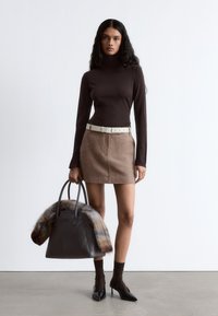 Brown turtleneck top, beige wool skirt, white belt, dark handbag with fur accent, and black pointed-toe heels. Smooth textures, modern design.