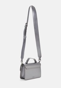 Bolso cruzado de cuero gris con correa ajustable, asa superior, cierre de solapa y un sutil logo en la parte frontal. Textura suave y diseño elegante.