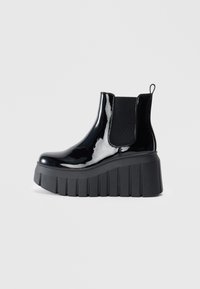 Černé lakované kožené kotníkové boty s elastickými bočními panely, masivní platformovou podrážkou a poutkem na zadní straně. Hladký povrch a elegantní design.