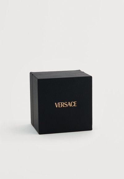 Μαύρο τετράγωνο κουτί με υφή στην επιφάνεια και χρυσό λογότυπο Versace στο κέντρο του μπροστινού μέρους, τοποθετημένο σε απλό λευκό φόντο.