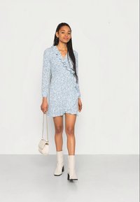 Φωτεινό μπλε φλοράλ φόρεμα με λεπτομέρειες ριπ, μακριά μανίκια και ρετούρ σχέδιο; συνδυασμένο με κρεμ τσάντα και μπεζ μπότες μέχρι τον αστράγαλο.