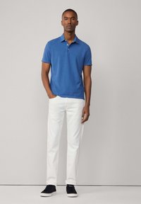 Camisa polo azul de manga corta con cuello, combinada con pantalones ajustados blancos y zapatillas oscuras. Diseño sencillo, sin patrones visibles.