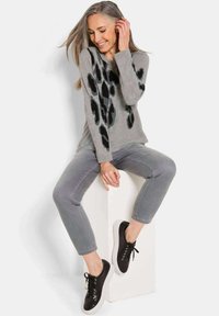 Maglione grigio con stampa leopardata nera, jeans grigi a vita corta e sneakers nere con suole bianche. Texture lisce, vestibilità rilassata.
