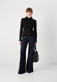 Zwarte geribbelde lange mouwen button-up shirt met een kraag, gecombineerd met donkerblauwe uitlopende jeans en een zwarte tote bag.