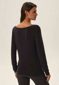 Schwarzes Langarmshirt mit weitem Halsausschnitt, das eine figurbetonte Form und eine glatte Textur aufweist. Zeigt Nähte an den Seiten und am Rücken.