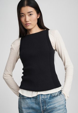 Débardeur noir à côtes superposé sur une chemise à manches longues crème, associé à un denim bleu clair, avec une silhouette ajustée et des lignes épurées.