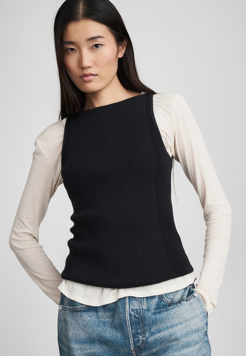 Débardeur noir à côtes superposé sur une chemise à manches longues crème, associé à un denim bleu clair, avec une silhouette ajustée et des lignes épurées.