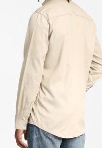 Beige Langarmhemd mit Schulterpasse, seitlichen Schlitzen und abgerundetem Saum. Aus einem weichen Stoff mit einer lockeren Passform.