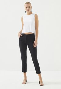 Witte geribbelde mouwloze top met een cropped ontwerp, gecombineerd met zwarte aansluitende broeken; doorzichtige sandalen met blokhak zichtbaar.