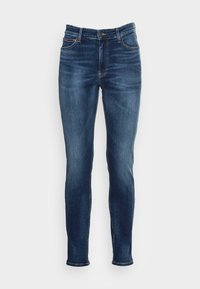 Slim-fit modré džíny s středním umytím, s pěti kapsami, zipovým zapínáním a jemnými detaily v šití, prezentované na bílém pozadí.