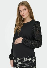 Mustmust musta, millel on tekstuuriga lille- ja sädelevad varrukad, ribidega mansetid ja ümmargune kaelus, koos musta lillemustriga seelikuga.