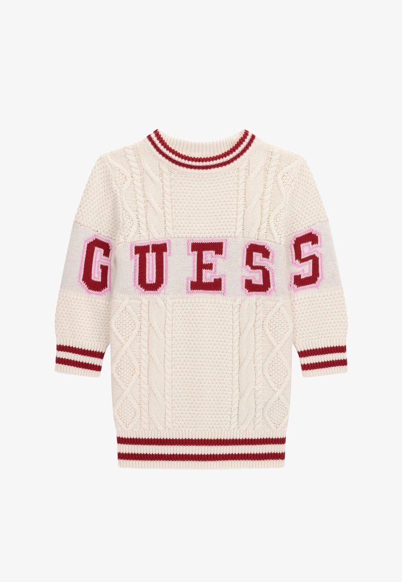 Pull en tricot crème avec motifs torsadés, col et poignets rayés rouges et blancs, avec "GUESS" en lettres rouges épaisses sur la poitrine et les manches.