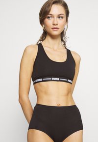 Zwarte sportbh met een elastische band met logo en bijpassende high-waisted slip. Zacht, rekbaar materiaal met een gladde textuur, mouwloos ontwerp.