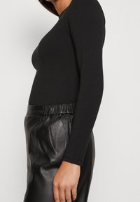 Musta pitkähihainen paita, valmistettu sileästä kankaasta, yhdistetty korkeavyötäröisiin mustiin nahkahousuihin, joissa on hillitty joustava vyötärönauha.