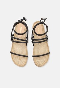 Sandales noires à brides avec une semelle en jute tissée. La tige présente plusieurs fines brides et une semelle intérieure plate et texturée avec un logo de marque.