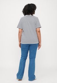 T-shirt rayé en coton bleu marine et blanc, manches courtes, coupe décontractée ; associé à un jean flare bleu clair et des baskets blanches.
