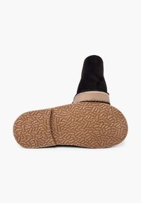 Botín de ante negro con una correa beige, que cuenta con una suela de goma marrón texturizada para mayor agarre. Sin patrones visibles ni acentos adicionales.