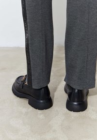 Gray trousers with a textured finish and a side stripe featuring black logo text, paired with black chunky-soled shoes.