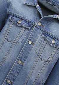 Lichtblauwe denimjacket met een knoopsluiting aan de voorkant, twee borstzakken met kleppen en een klassieke kraag. Gestructureerde stof met vervagingdetails.