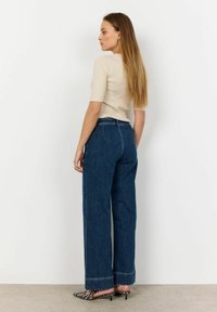 Beige ribbat kortärmad topp tillsammans med mörkblå vida jeans, med rak skärning och uppvikta fållar. Svartvita randiga klackar.