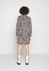 Langärmliges Kleid mit schwarz-weißem Blumenmuster, knielang, mit hohem Kragen und elastischen Bündchen. Getragen mit weißen Stiefeletten.