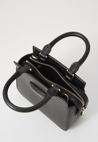 Sac à main en cuir noir avec double poignée supérieure, quincaillerie dorée et fermeture éclair. Dispose d'un compartiment zippé et d'un logo à l'avant.