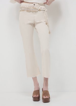 Jean en denim évasé de couleur crème avec ourlet effiloché, orné d'une ceinture chaîne décorative. Associé à des sandales à semelle plateforme marron.