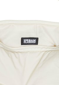 Close-up of a white fabric bag with a zipper and a black label reading "Urban Classics" inside the opening.