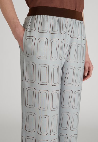 Pantalons bleu clair avec un motif rectangulaire brun répété, taille élastique, poches latérales et une finition en tissu lisse légèrement texturée.
