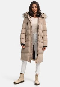 Beige Daunenjacke mit einem gefütterten Kapuzenrand, Reißverschluss vorne, Seitentaschen und gerippten Bündchen. Tragen über einem leichten Pullover und kombiniert mit weißen Jeans und beigen Stiefeln.