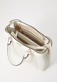 Lyse beige taske med guld hardware, dobbel top håndtag og lynlås lukning. Indvendigt har den flere rum og en glat tekstur.