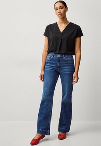Sort bluse med korte ærmer og v-hals, parret med høj-tskåret blå jeans og røde ruskindssko. Enkel, moderne design; glat tekstur.