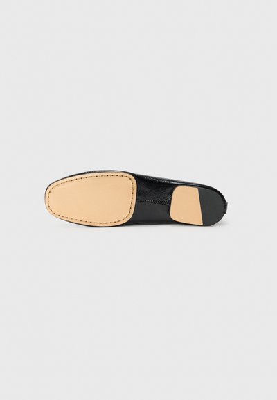 Semelle de chaussure noire avec une finition lisse, une forme arrondie et des accents beiges. Détails de couture le long du bord pour plus de structure.